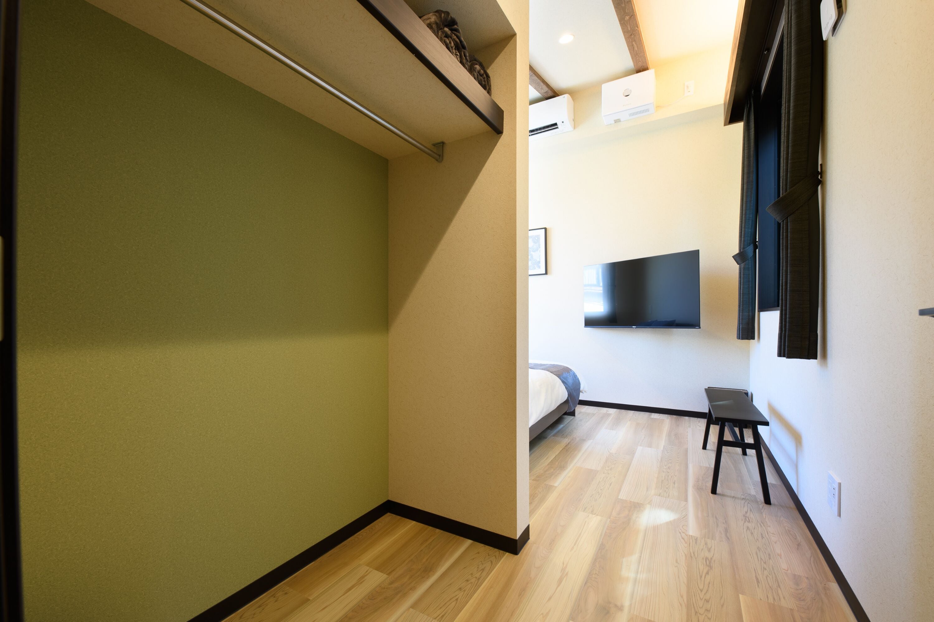 A narrow hallway with a wooden floor, a bed in the background, and a TV mounted on the wall.