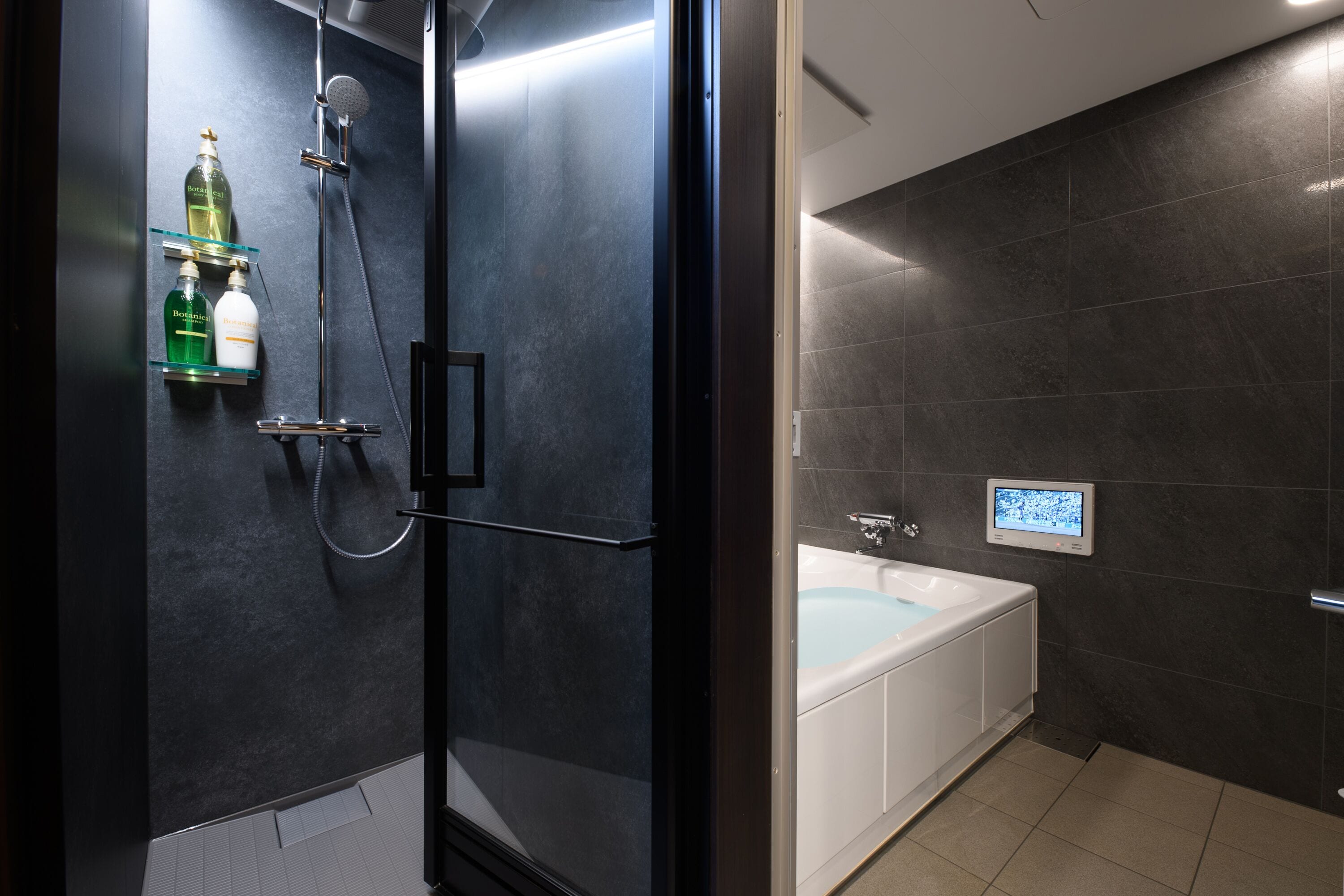 A modern bathroom with a glass-enclosed shower, a white bathtub, and a digital control panel.
