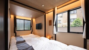 Habitación de hotel con una cama grande, una ventana con cortinas, un televisor montado en la pared y una mesita de noche con lámpara.