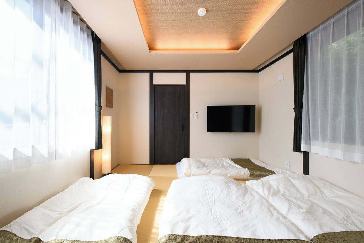 A hotel room with two beds, a flat-screen TV mounted on the wall, and a door in the center.