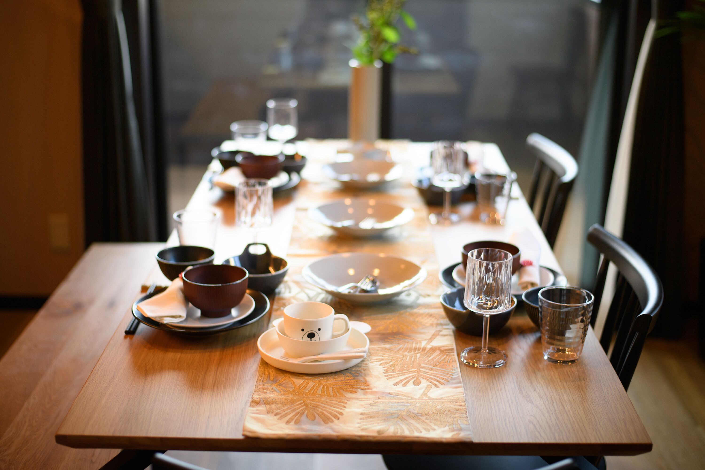 A dining table set with various dishes and glasses, a vase with a plant, and a window in the background.