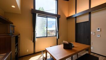 Una habitación con una mesa de madera, sillas, un ventanal con cortinas, un horno empotrado y una puerta de madera oscura.