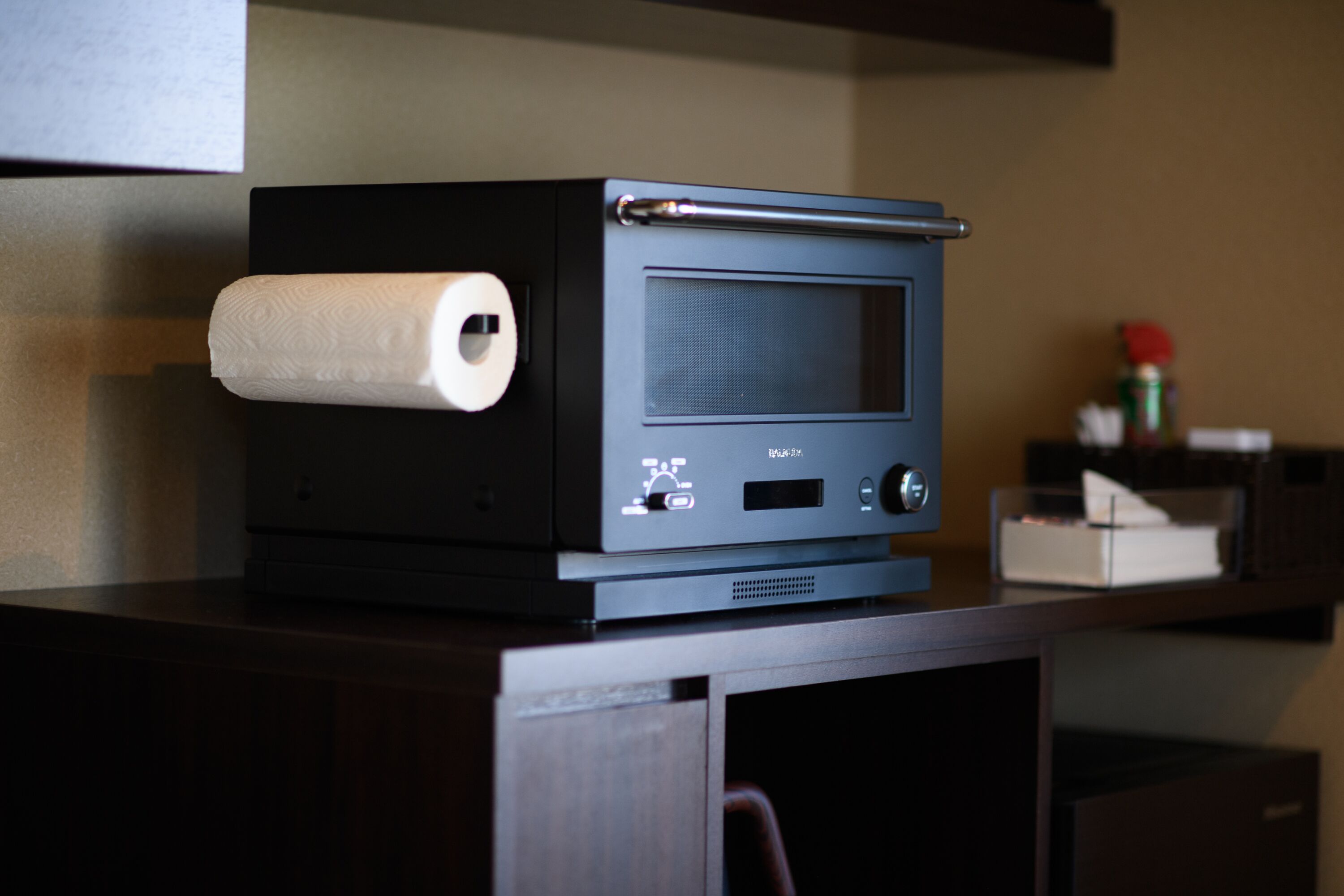 A microwave oven on a wooden countertop with a roll of paper towels and a can of soda in the background.
