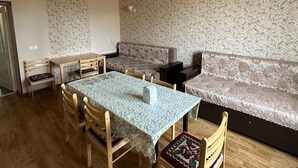 A dining area with a table, chairs, a sofa, and a ceiling light fixture. - Zhenja and Lyuda's Boarding House (Zhabagly)