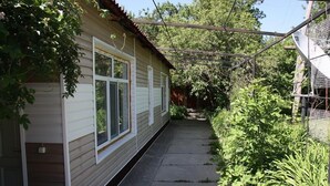 A narrow concrete pathway flanked by a house with white siding and a metal fence. - Zhenja and Lyuda's Boarding House (Zhabagly)