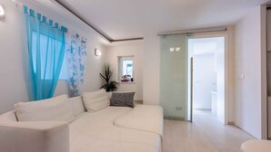 Een moderne woonkamer met een witte bank, een klein bijzettafeltje, een potplant en een schuifdeur naar een balkon.