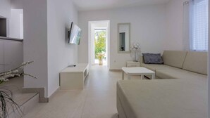 Un salon moderne et minimaliste, avec un canapé, une table basse et un téléviseur fixé au mur. On y trouve également une petite table avec une lampe et un miroir accroché au mur.