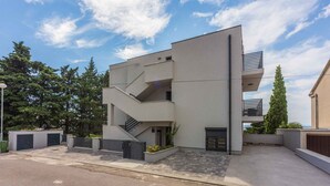 Un immeuble moderne à plusieurs étages, doté d’un toit plat, d’un escalier menant à l’étage supérieur et d’une entrée fermée par un portail.