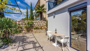 Une terrasse extérieure moderne avec un mur en pierre, des chaises blanches et une table sur laquelle se trouve une bouteille.