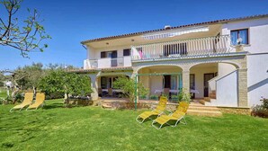 A two-story house with a balcony, a covered porch, and a well-maintained lawn with two lounge chairs.