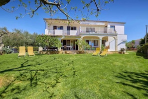 Une maison à deux étages avec un balcon, une pelouse agrémentée de deux chaises longues et un petit jardin.