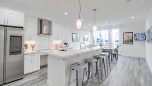 A modern kitchen with white cabinetry, stainless steel appliances, and a central island with bar stools. - Park Blvd 302 | Newly Built | Spa | Central (San Diego)