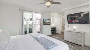 A hotel room with a bed, a TV mounted on the wall, a ceiling fan, and a desk with a chair. - Park Blvd 302 | Newly Built | Spa | Central (San Diego)