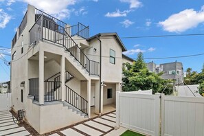 Una casa de dos pisos con escaleras, un balcón y una cerca blanca.
