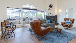 Ein geräumiges Wohnzimmer mit einem großen Glasfenster, das zu einem Außenbereich führt, eine Couch, zwei Ledersessel und ein Couchtisch.