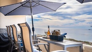 Ein Balkon mit Sitzgelegenheit im Freien, einem Grill und einem Tisch mit Flasche und Korb.