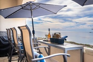 A balcony with outdoor seating, a grill, and a table with a bottle and basket. - Sunset Serenity On The Cliffs | Balcony| Oceanview (San Diego)
