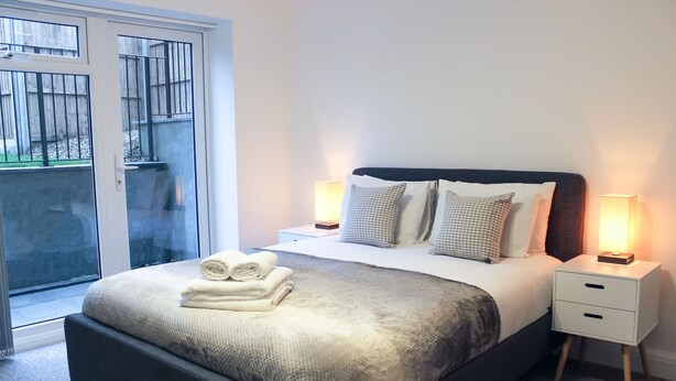 A bedroom with a bed, bedside tables, and a sliding glass door to an outdoor area. - West Finchley by Viridian Apartments (London)