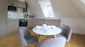 A modern kitchen with a dining area, featuring a round table with chairs, a built-in oven, and a window providing natural light. - West Finchley by Viridian Apartments (London)