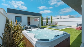 A modern outdoor hot tub area with a pool, seating, and a well-maintained lawn.