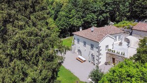 Un bâtiment blanc, surmonté d’un toit en tuiles, entouré d’une végétation luxuriante.