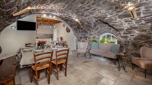 Un coin repas rustique aux murs de pierre, avec une table dressée pour quatre personnes, un canapé agrémenté de coussins à carreaux et une petite table d’appoint sur laquelle est posée une bougie.