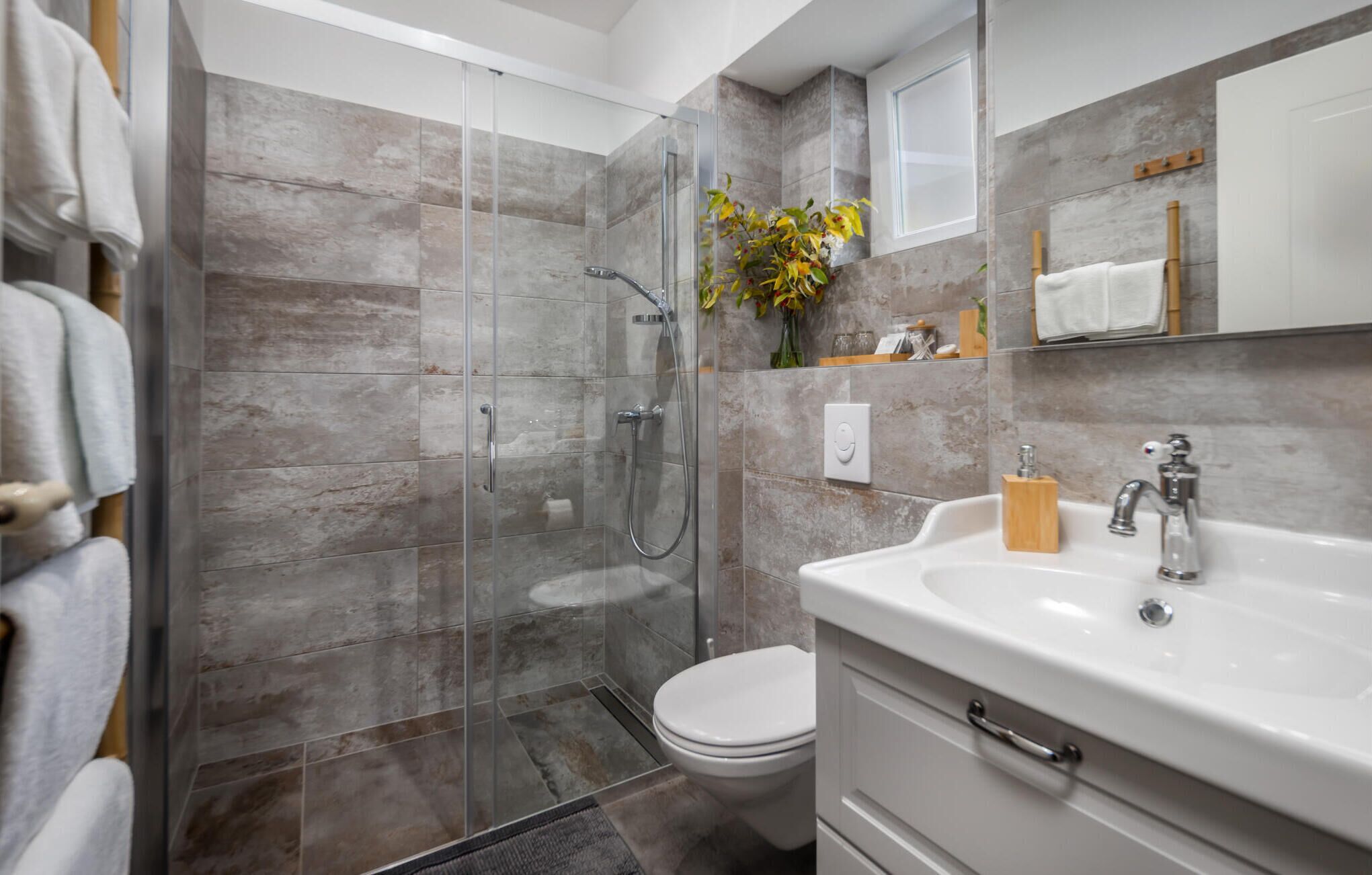 Ein modernes Badezimmer mit einer Glaskabine für die Dusche, einer weißen Toilette und einem Waschbecken mit einem Holz-Seifenschälchen.