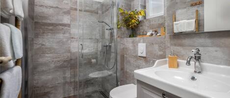 Ein modernes Badezimmer mit einer Glaskabine für die Dusche, einer weißen Toilette und einem Waschbecken mit einem Holz-Seifenschälchen.