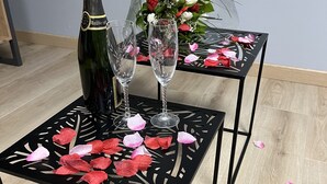 Una mesa con una botella y copas, rodeada de pétalos de rosa.
