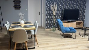 Una sala de estar moderna con comedor, que incluye un televisor, un sillón azul y un panel decorativo en la pared.