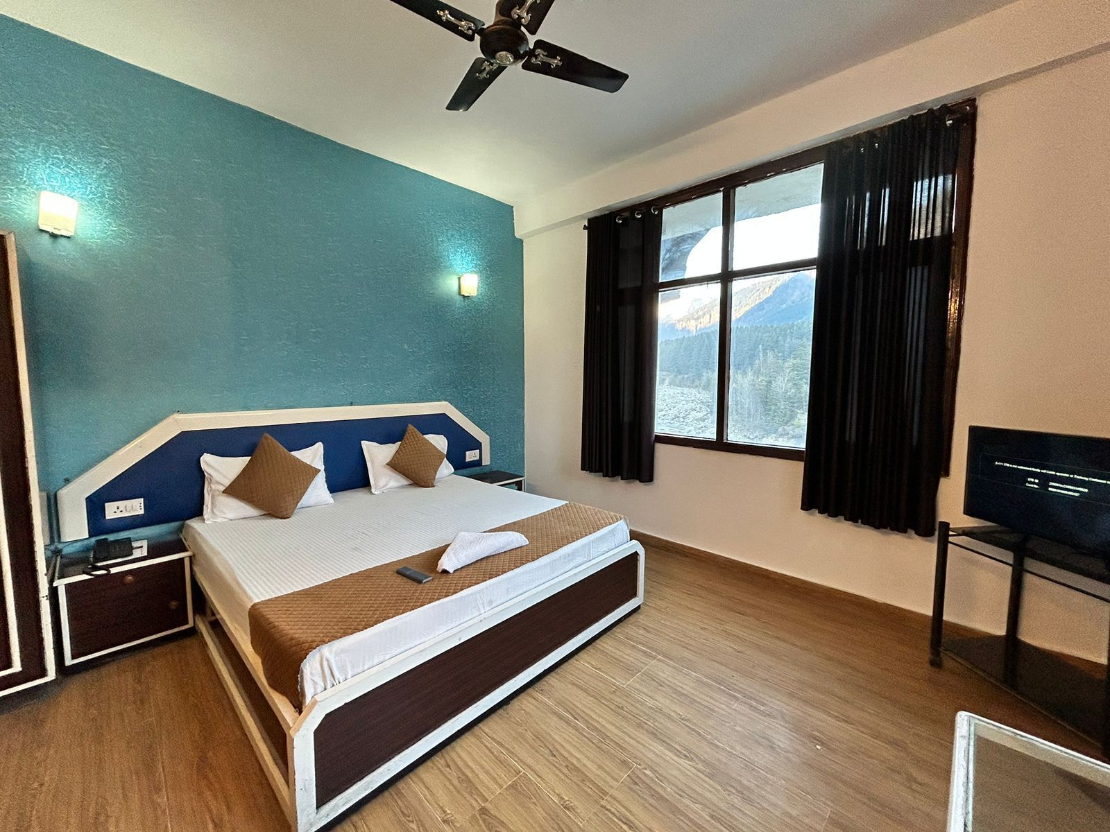 A hotel room with a bed, a ceiling fan, a TV, and a window with curtains.