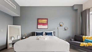 A modern hotel room with a large bed, a bedside table, a mirror, and a gray sofa. - WelHome - Greenery Beautiful Apartment Onyx Tower 2 (Dubai)