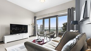 A modern living room with a large TV, comfortable seating, and a city view. - WelHome - Greenery Beautiful Apartment Onyx Tower 2 (Dubai)