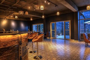 Zona de bar con mostrador de madera, taburetes de cuero y lámparas colgantes.