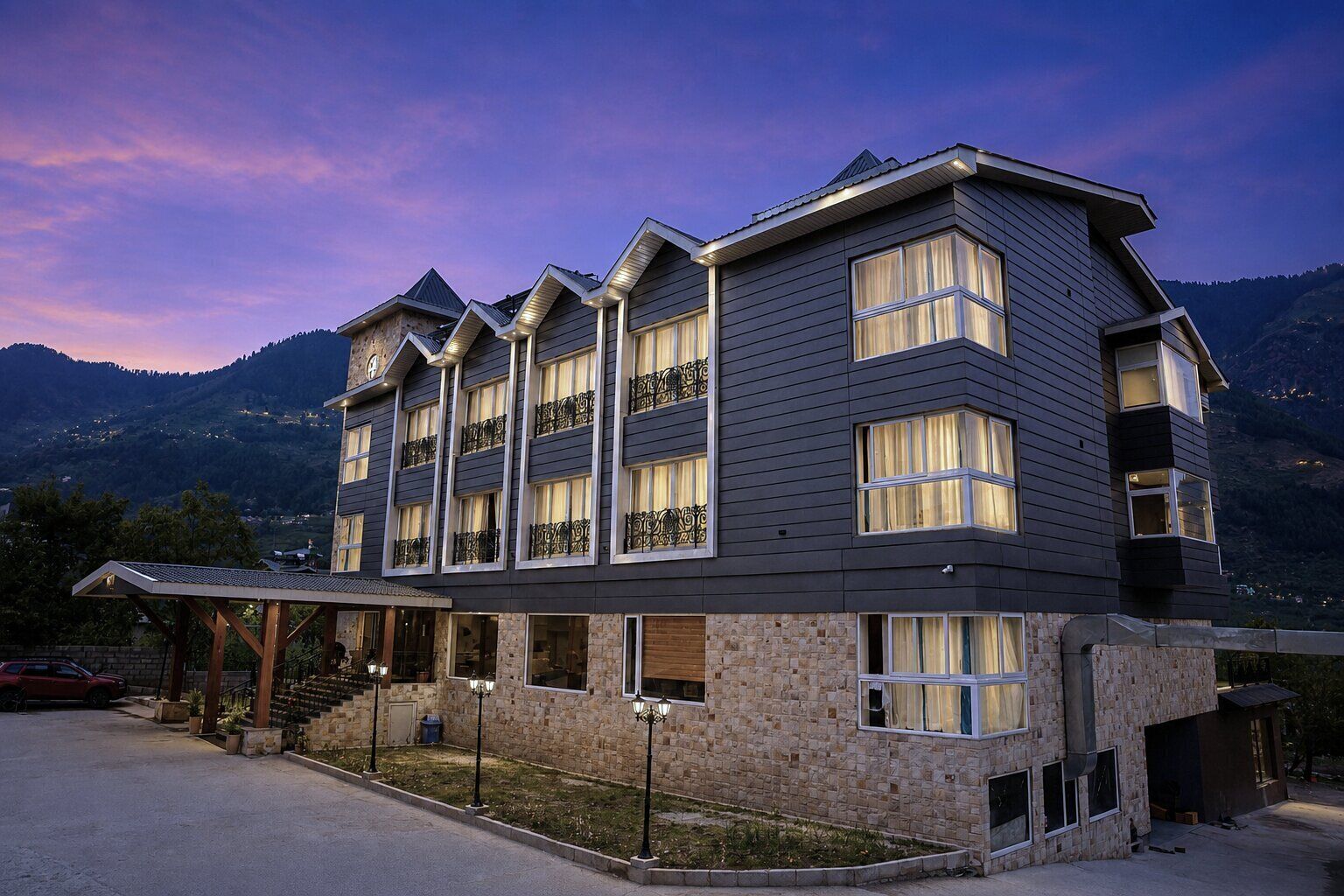 Un hotel de varios pisos con fachada de piedra, múltiples balcones y vista a las montañas.