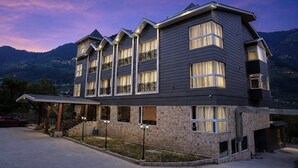 A multi-story hotel with a stone facade, multiple balconies, and a view of the mountains. - The Voyage Resort, Manali (Manali)