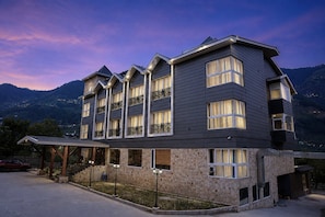 A multi-story hotel with a stone facade, multiple balconies, and a view of the mountains. - The Voyage Resort, Manali (Manali)