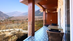 Un balcone con vista sulle montagne, travi in legno e un tavolo in vetro con sedie.