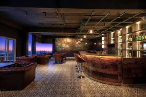 A bar area with a curved wooden counter, leather seating, and a city view through large windows. - The Voyage Resort, Manali (Manali)