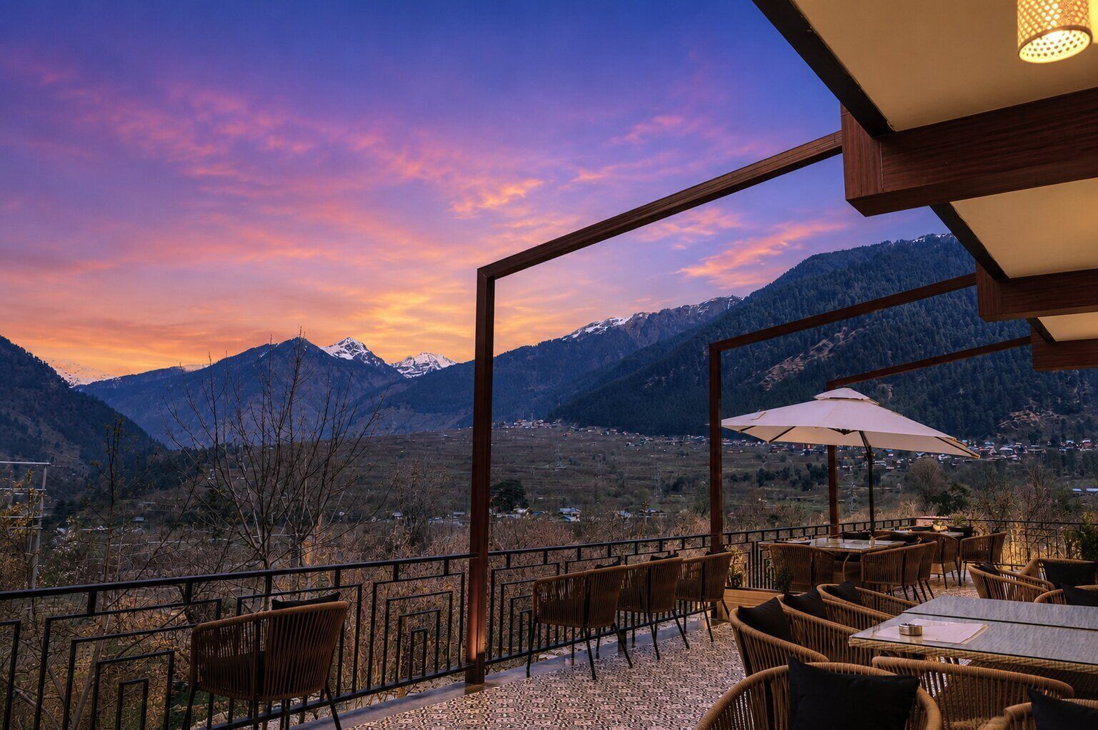 An outdoor seating area with wicker furniture, a table, and an umbrella, overlooking a mountainous landscape.