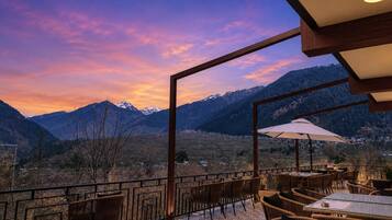 An outdoor seating area with wicker furniture, a table, and an umbrella, overlooking a mountainous landscape.