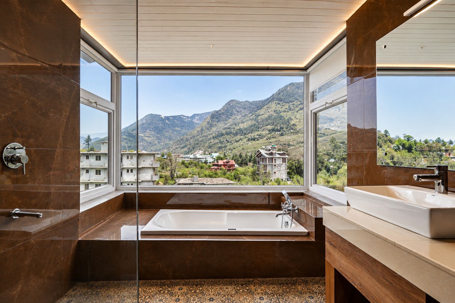 Un baño moderno con una bañera grande, dos lavamanos y vistas a un paisaje montañoso a través de amplias ventanas.