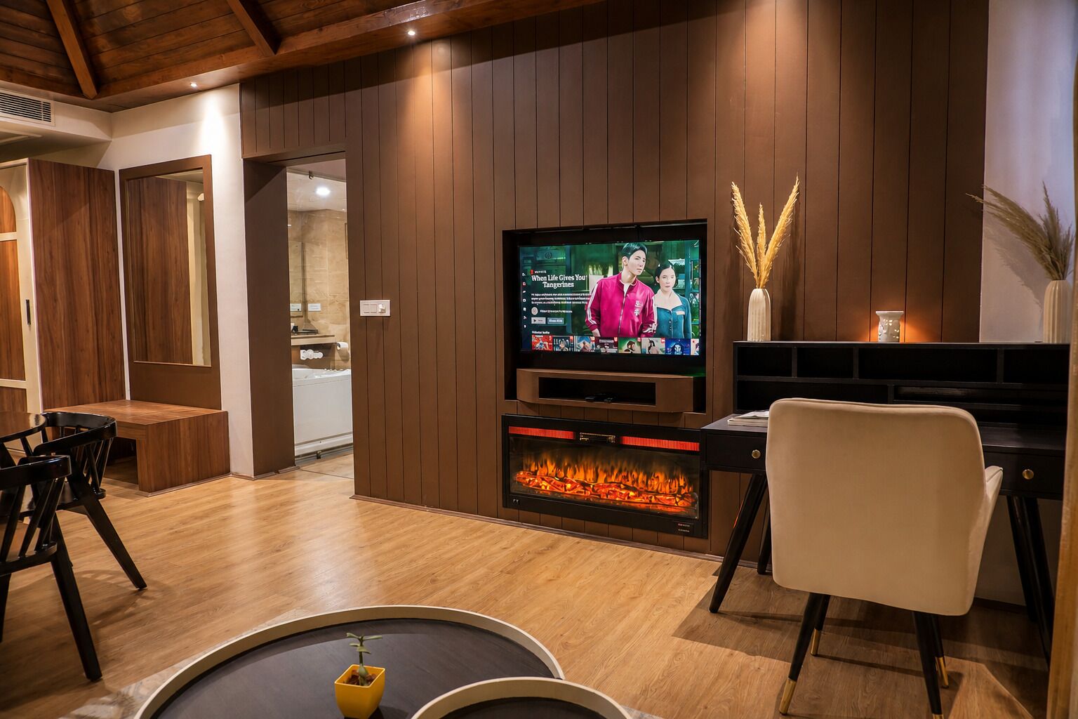 A modern living room with a flat-screen TV, a fireplace, wooden flooring, and a dining area.
