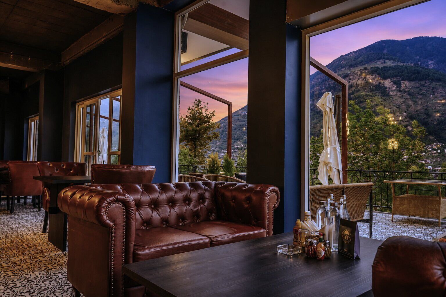 A cozy lounge area with a leather sofa, a dining table, and a view of a mountainous landscape through large windows.