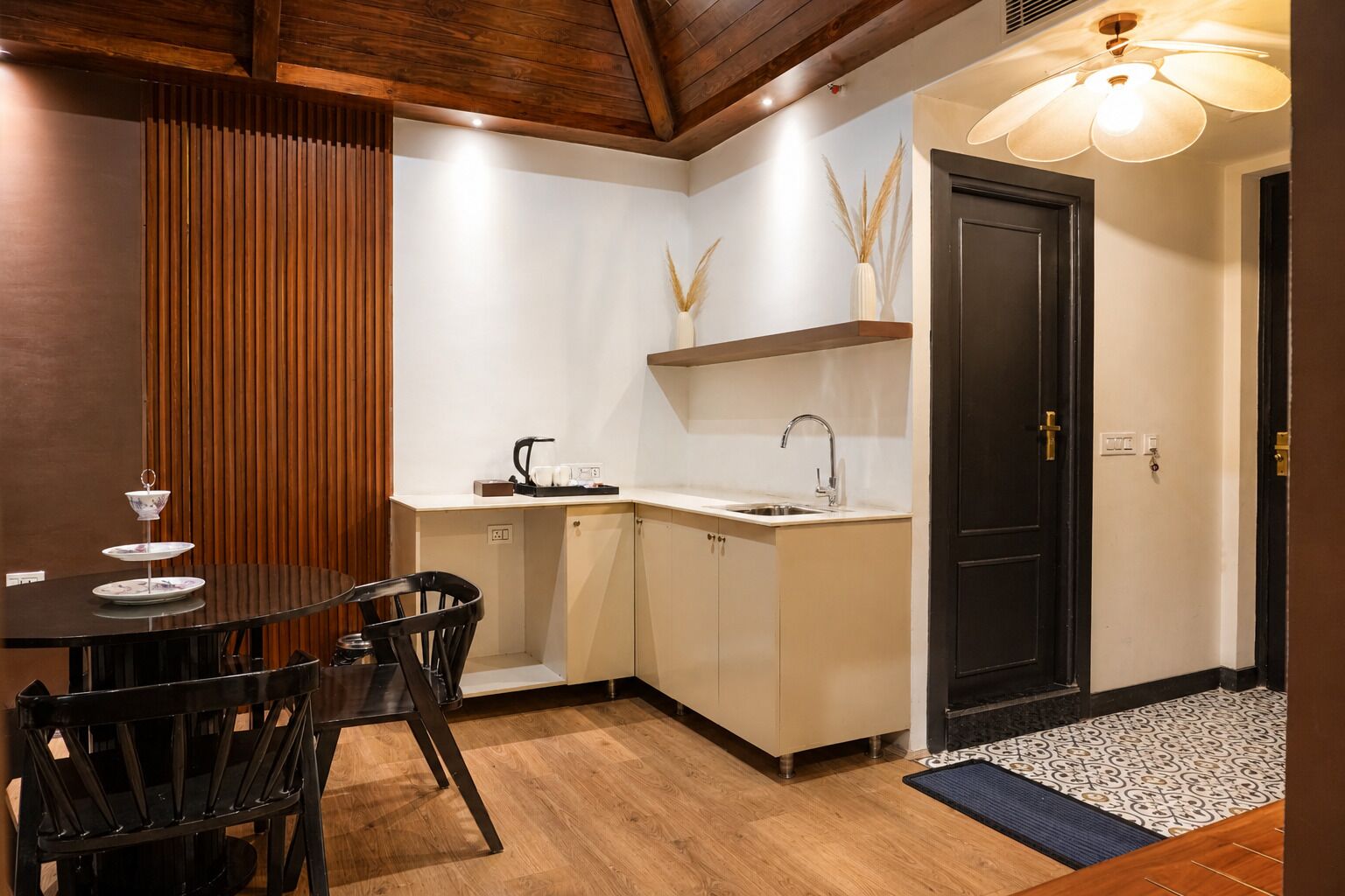 A compact kitchen with a dining area, featuring a wooden ceiling, a black door, and a small countertop with a kettle.