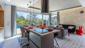 A modern kitchen with a central island, dining area with chairs, a sofa, and a stone wall. - Villa with modern equipment and swimming pool (Crikvenica)