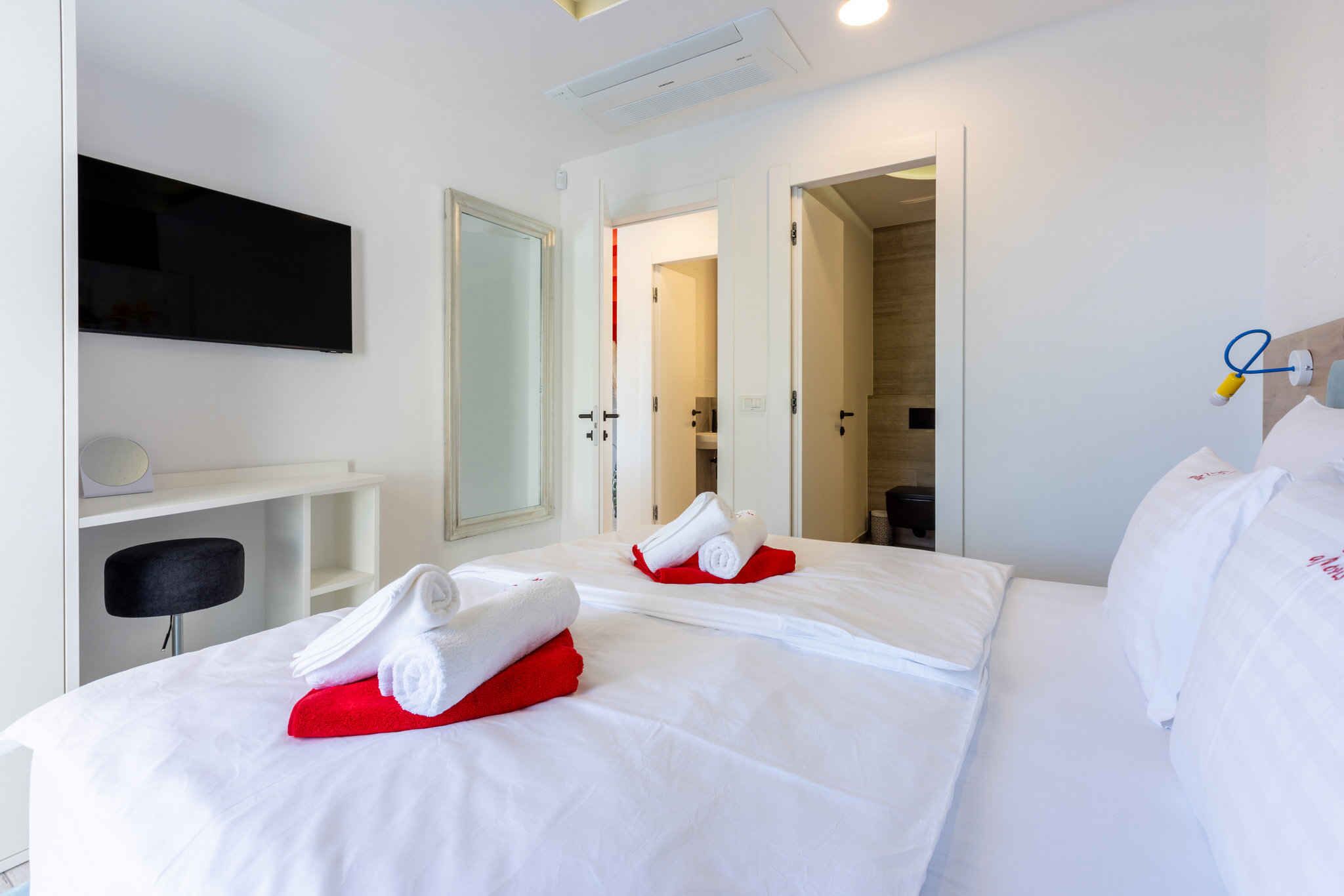 Ein Hotelzimmer mit zwei Betten, einem Flachbildfernseher, einem Schreibtisch und einem Spiegel.