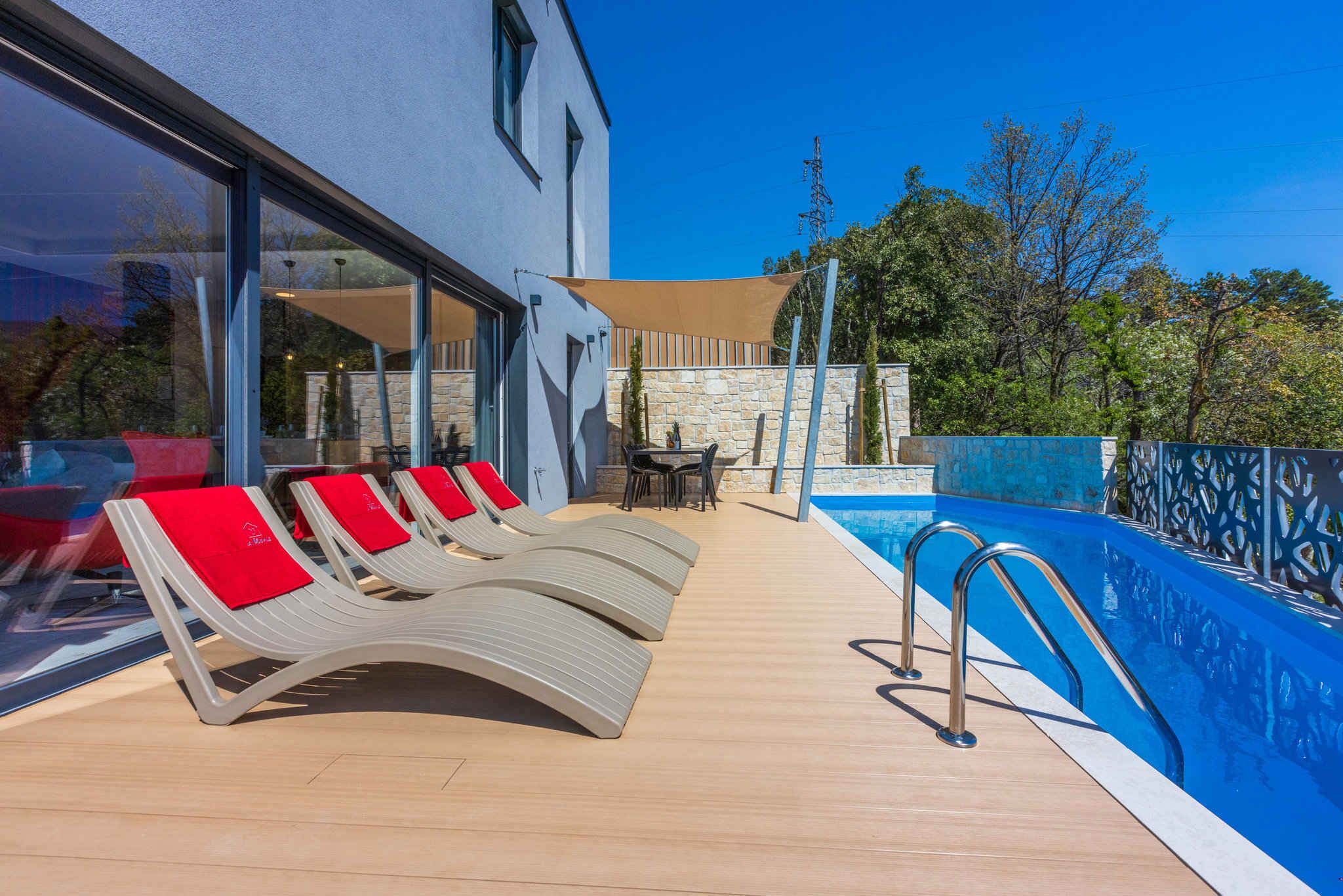 A poolside area with lounge chairs and a table, a swimming pool, and a building with large windows.