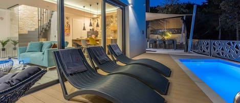 A modern outdoor living area with a pool, lounge chairs, and a dining area.