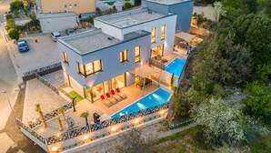 Ett modernt hus i två våningar med en swimmingpool, en uteplats och utsikt över det omgivande landskapet.